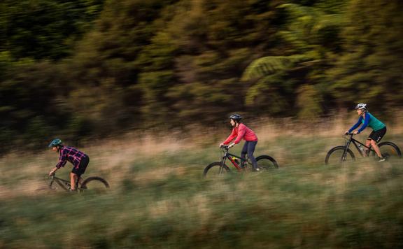 Three cyclists ride down a grassy hill.