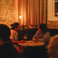 Two people converse over a glass of wine in the corner booth at Puffin wine bar, a natural wine and cocktail bar in Te Aro, Wellington.