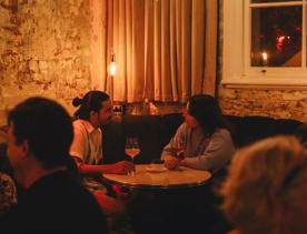 Two people converse over a glass of wine in the corner booth at Puffin wine bar, a natural wine and cocktail bar in Te Aro, Wellington. 