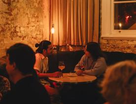 Two people converse over a glass of wine in the corner booth at Puffin wine bar, a natural wine and cocktail bar in Te Aro, Wellington.