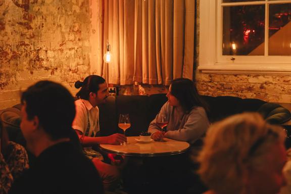 Two people converse over a glass of wine in the corner booth at Puffin wine bar, a natural wine and cocktail bar in Te Aro, Wellington.