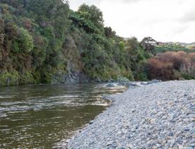 The Taitā Rock swimming hole in Lower Hutt, with lush green bush surrounding a blue river and large pebbles on the shore.