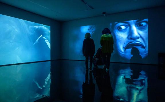 2 people looking at a projected art piece on the wall of Pātaka Art + Museum.