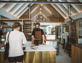 A person is paying for their order at the counter of Baker Gramercy, a bakery in Upper Hutt. The interior has a modern, minimalist feel with white walls and light wooden accents.