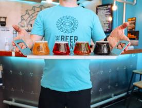 Staff member holding a tasting tray of 4 different coloured beers with the Beer engine logo on them.