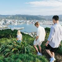 Three people walking at the summit of Mount Victoria with a view of Wellington city in the background.