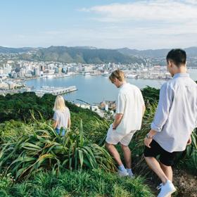 Three people walking at the summit of Mount Victoria with a view of Wellington city in the background.