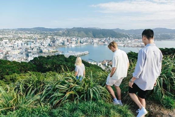 Three people walking at the summit of Mount Victoria with a view of Wellington city in the background. 