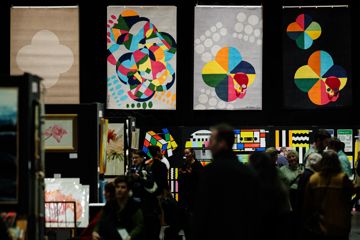 A busy exhibition with brightly coloured artwork on dark walls.