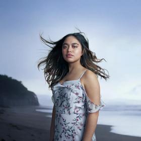 A person wearing a floral dress stands on a windy beach.