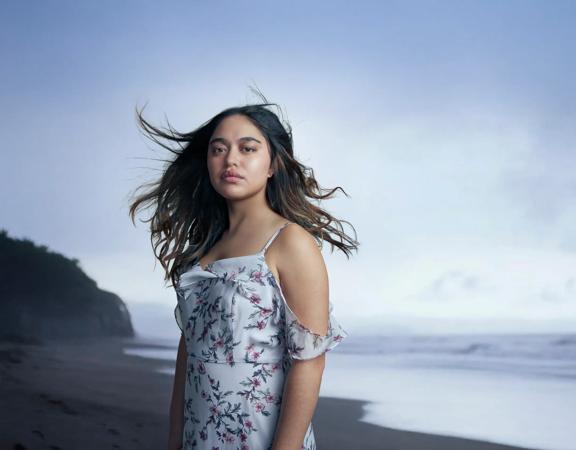 A person wearing a floral dress stands on a windy beach.