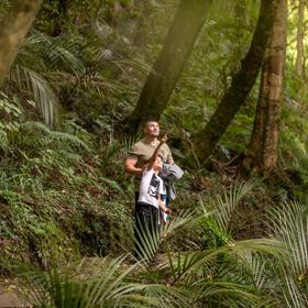 A child and adult in the bush looking into the trees and pointing.