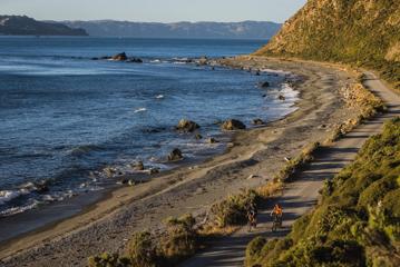 2 bikers on Pencarrow Coast Road, with the Wellington Harbour in the background.