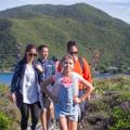 A family walks through kapiti island with green bush and blue water surrounding them.