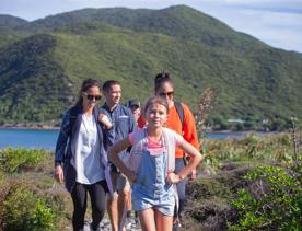 A family walks through kapiti island with green bush and blue water surrounding them.