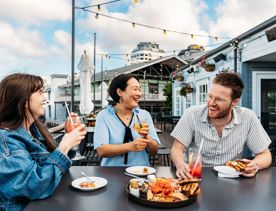Three people sit at a bar table at Foxglove Bar on the Wellington Waterfront. They are all drinking a cocktail and a charcuterie board sits between them.