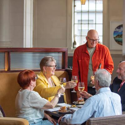 A group of 5 people clink their glasses on the sofa seats inside Logan Brown.