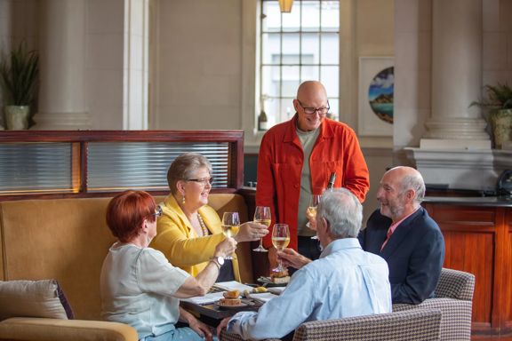 A group of 5 people clink their glasses on the sofa seats inside Logan Brown.