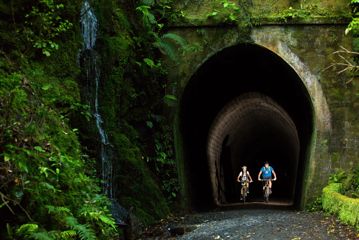 Two bikers going through a dark tunnel on the Rail Trail Section on the Remutaka Cycle Trail.