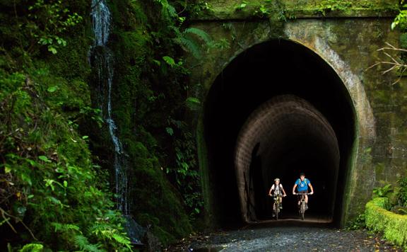 Two bikers going through a dark tunnel on the Rail Trail Section on the Remutaka Cycle Trail.
