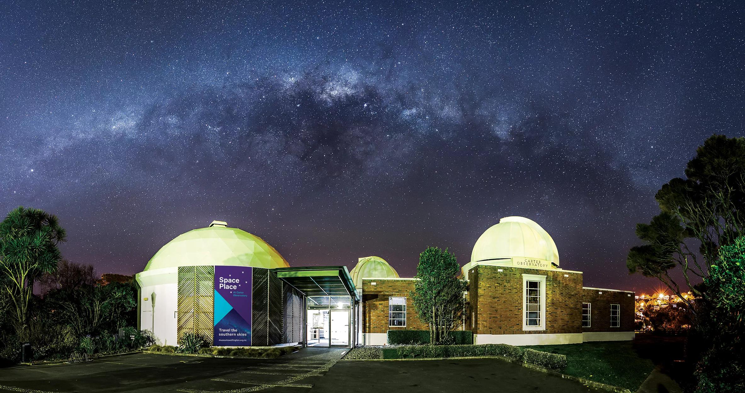 The exterior of Space Place observatory, at night. the stars of the Milky Way are seen above with purple hues. 