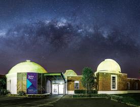 The exterior of Space Place observatory, at night. the stars of the Milky Way are seen above with purple hues.