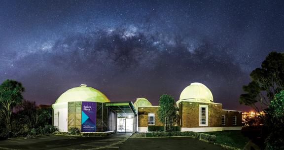 The exterior of Space Place observatory, at night. the stars of the Milky Way are seen above with purple hues.