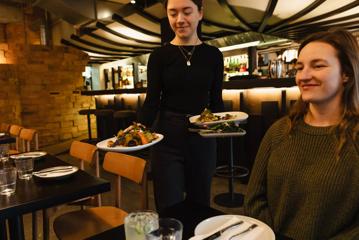 A server wearing all black carries three plates to a table at a restaurant.