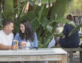 Two people sit at a table enjoying drinks on a restaurant patio.