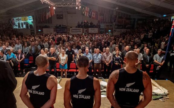 Image from The Golden Shears competition Three people stand on stage facing a full audience.