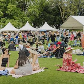 Groups of people sit on picnic blankets on a grassy field.