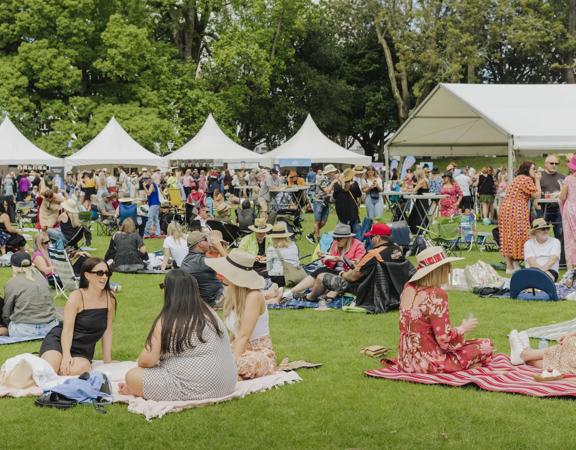 Groups of people sit on picnic blankets on a grassy field.