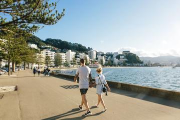 Two people hold hands while walking along Oriental Parade in Wellington, New Zealand.