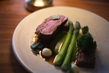 A dish with steak, cooked rare, two asparagus and sauces on a plate.