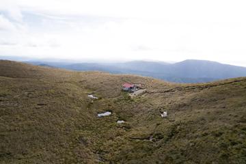 Kime Hut in Tararua Forest Park sits on a grassy mountain top under a foggy sky. 