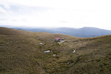 Kime Hut in Tararua Forest Park sits on a grassy mountain top under a foggy sky.