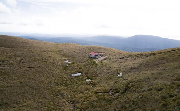 Kime Hut in Tararua Forest Park sits on a grassy mountain top under a foggy sky.