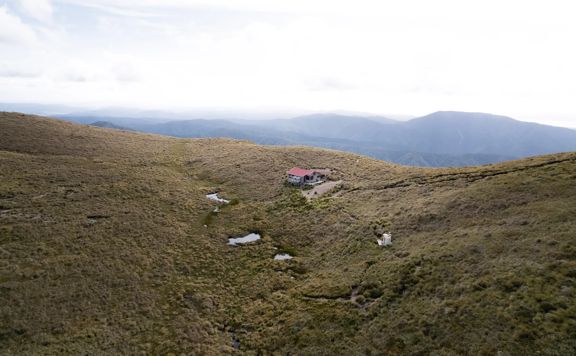 Kime Hut in Tararua Forest Park sits on a grassy mountain top under a foggy sky.