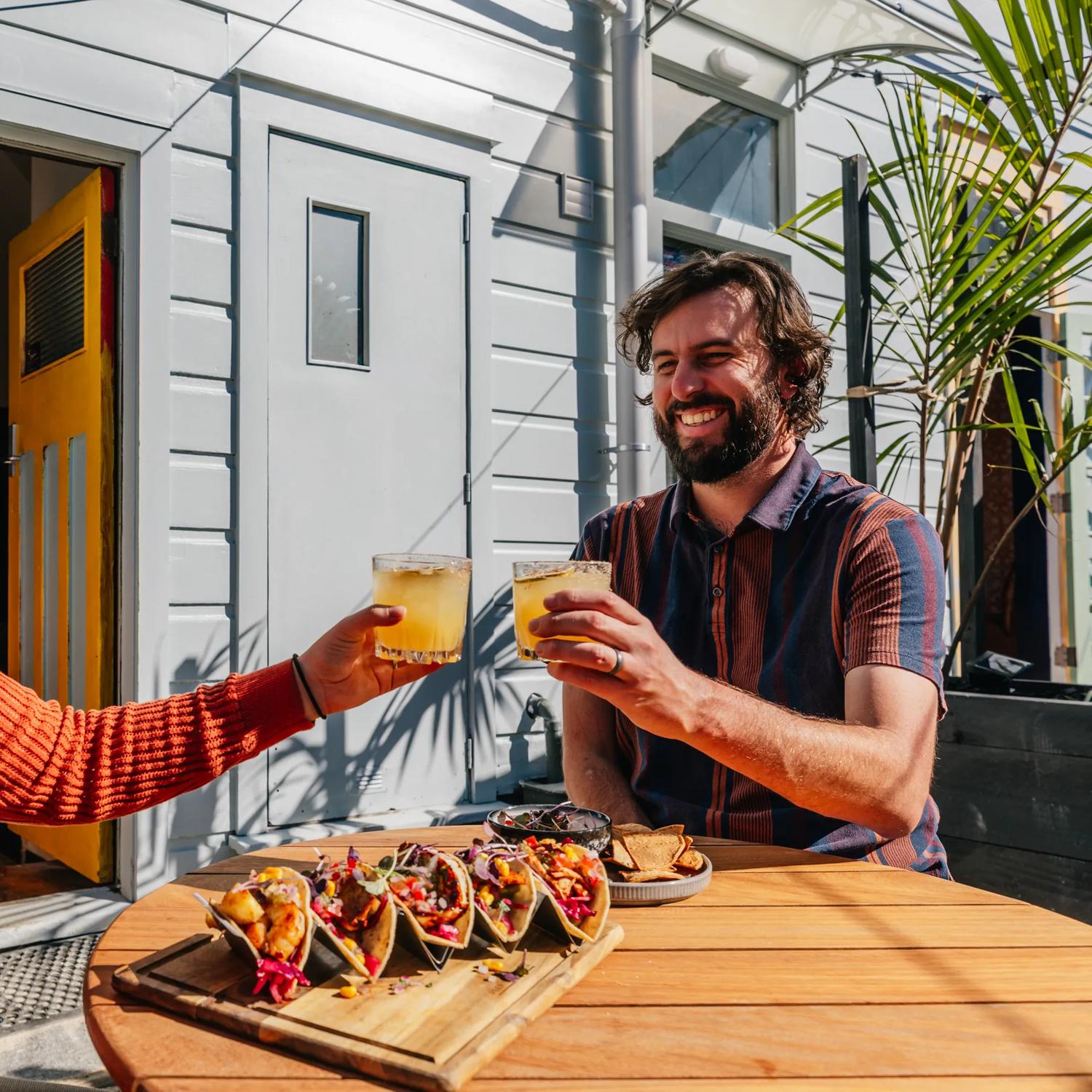 Two friends raise their glasses on the sunny patio at Superfina on Cuba Street.