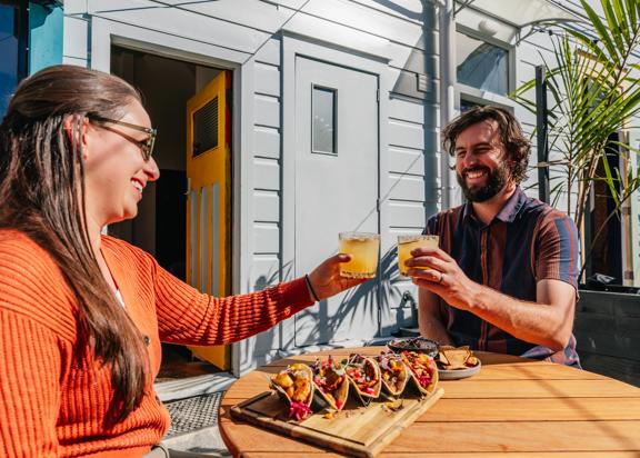 Two friends raise their glasses on the sunny patio at Superfina on Cuba Street.