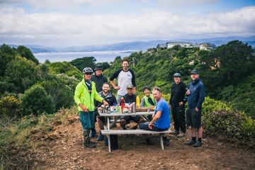 A group of track-builders take a break and enjoy tea and snacks at a picnic table on a hilltop.