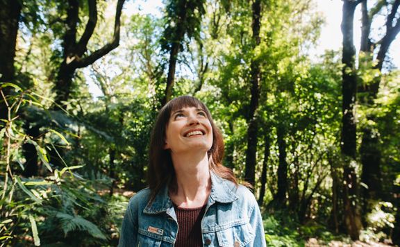 Person in Ōtari-Wilton's Bush smiling up at the sky, surrounded by native trees.