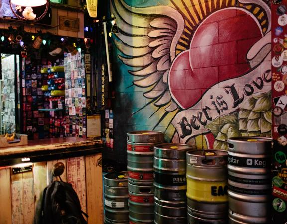 The interior of Golding’s bar. Kegs are stacked against the concrete brick wall, which has been painted with a heart with wings and a banner across it that says ‘beer is love’.