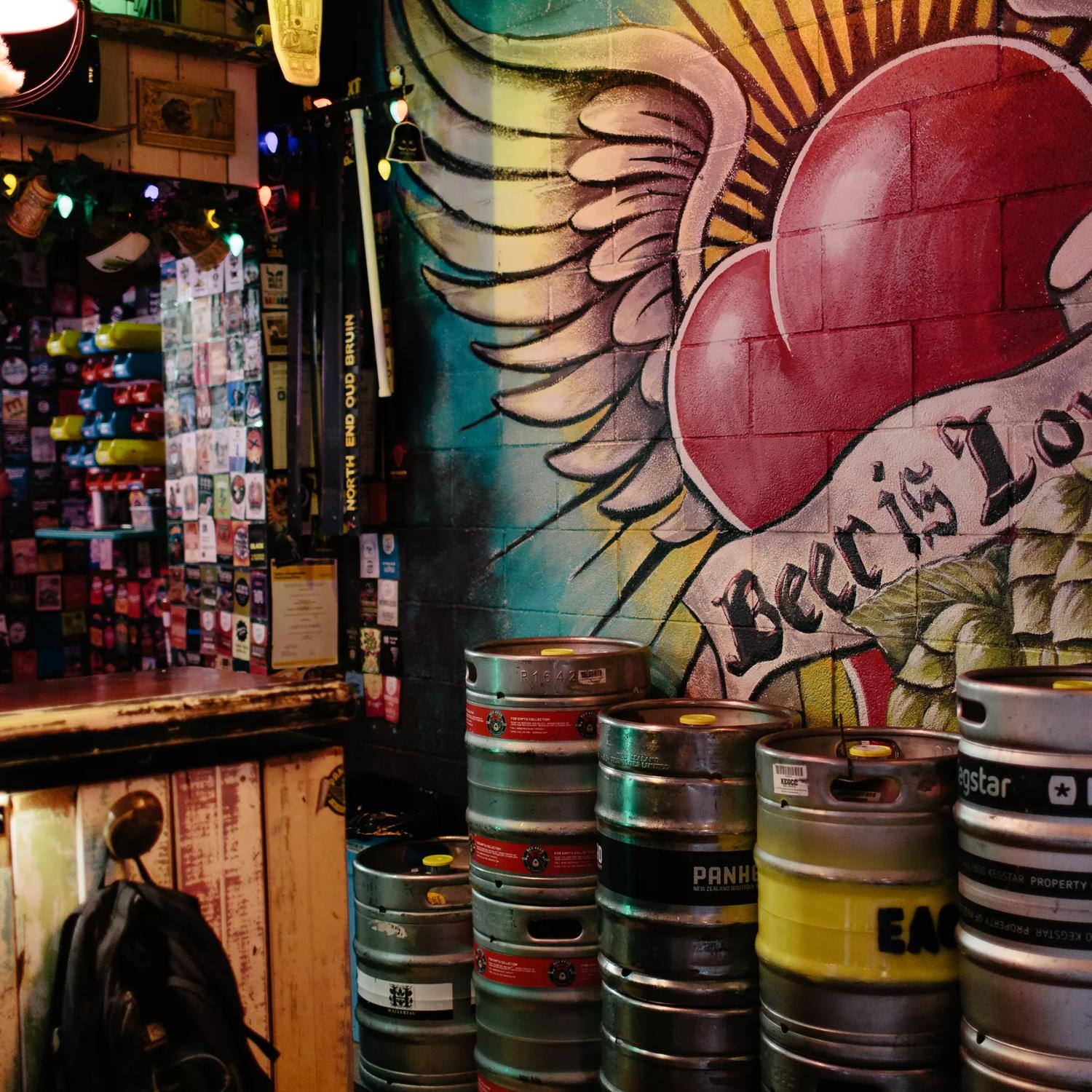 The interior of Golding’s bar. Kegs are stacked against the concrete brick wall, which has been painted with a heart with wings and a banner across it that says ‘beer is love’.
