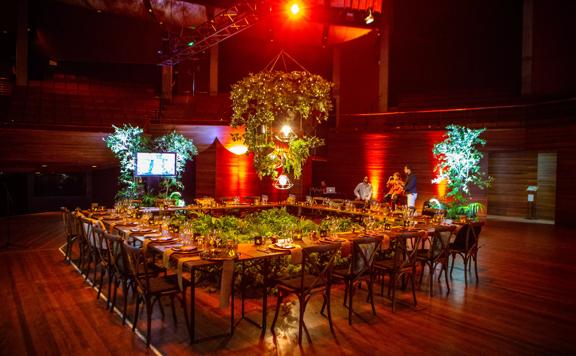A stage set up at the Michael Fowler Centre in Wellington. Tables are arranged into a square with space in the centre for green foliage.
