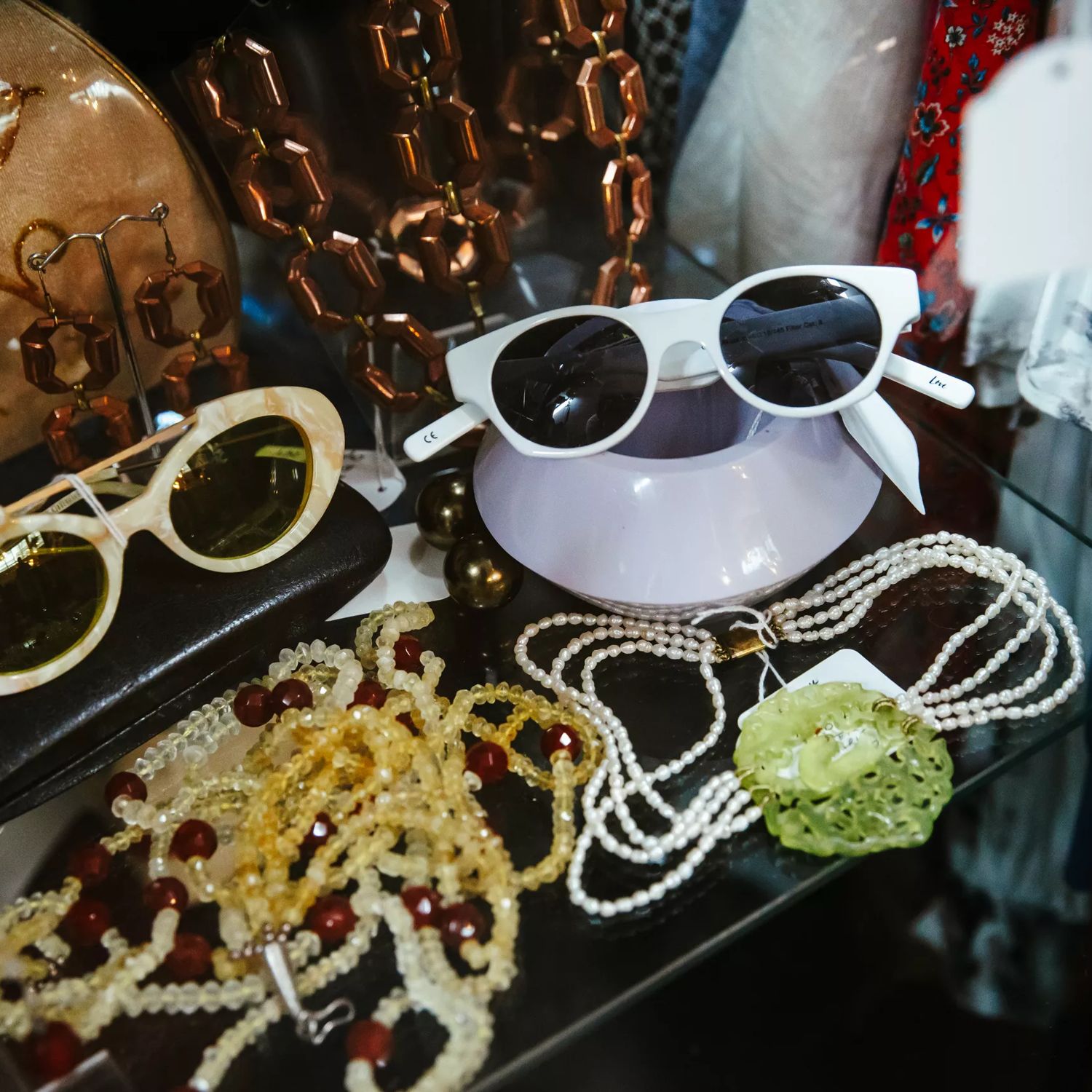 A glass shelf in a secondhand store with beaded necklaces and vintage sunglasses.