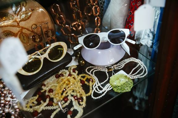 A glass shelf in a secondhand store with beaded necklaces and vintage sunglasses.