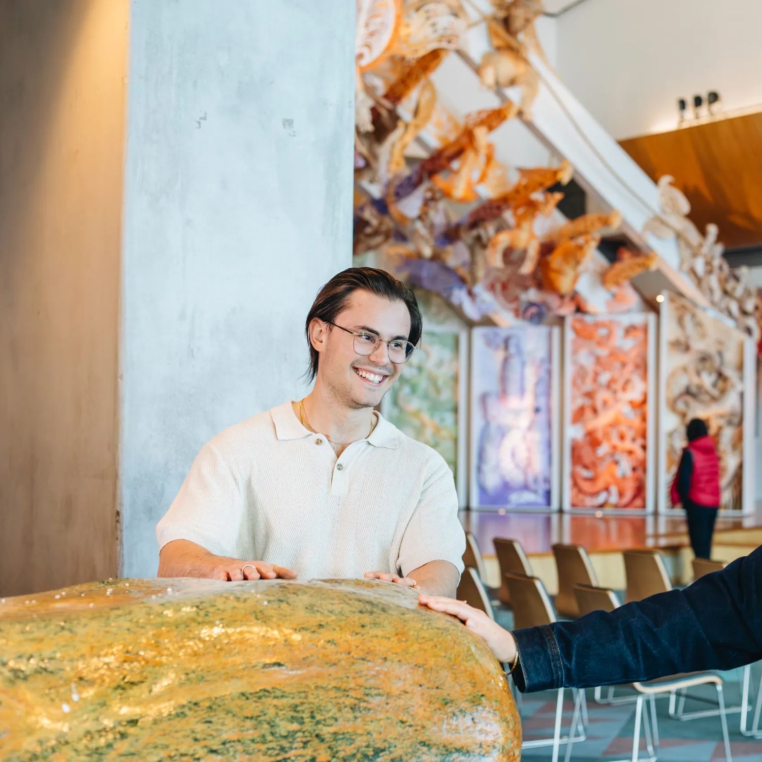 Two people touching a large rock at Museum of New Zealand Te Papa Tongarewa with the marae in the background.