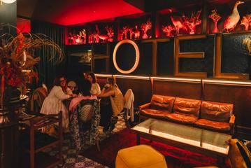 Four people sit at a round table in the lobby of the Intrepid Hotel on Ghuznee Street in Wellington. The room has red lighting, taxidermy birds and dry flowers as decoration and wood-paneled walls.