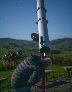 A person looks through a telescope at the stars at dusk.